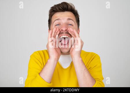 Aufgeregter junger weißer Mann, der schreit und Hände um den Mund legt Stockfoto