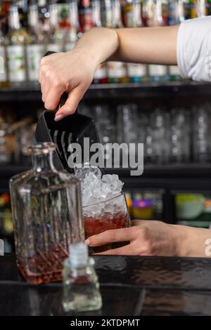 Barkeeperin, die zerstoßenes Eis mit einer speziellen Schaufel in Glas auf der Theke gießt. Ein Bestandteil der beruflichen Tätigkeit eines Barkeepers. Stockfoto