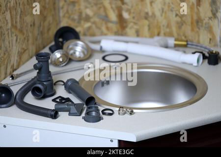 Sanitär-Werkzeuge und Wasserhahn bereit für die Installation in der Nähe des Waschbeckens auf der Arbeitsfläche in der Küche. Anschlüsse für die Installation des Wasserhahns für das Küchenspüle Stockfoto