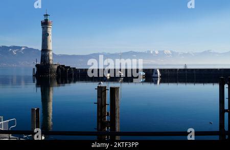 Hafen von Lindau am ruhigen, winterlichen Bodensee oder Bodensee mit den Alpen im Hintergrund an einem schönen Winterabend mit malerischem Himmel Stockfoto