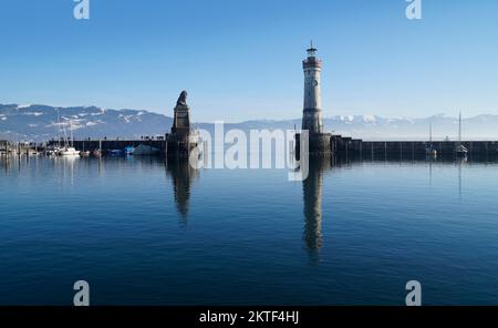 Hafen von Lindau am ruhigen, winterlichen Bodensee oder Bodensee mit den Alpen im Hintergrund an einem schönen Winterabend mit malerischem Himmel Stockfoto