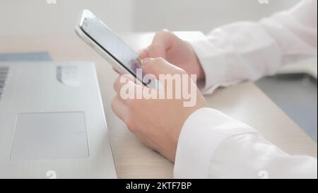 Am Arbeitsplatz mit Smartphone, SMS, Auswahl und Kauf von Waren und Dienstleistungen online, Konzept der Nutzung moderner Technologie. Nahaufnahme von weiblichen Händen, die halten Stockfoto