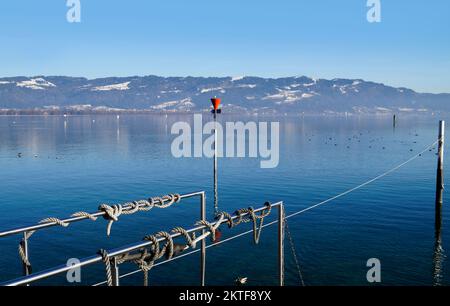 Hafen der Insel Lindau am ruhigen Bodensee oder Bodensee mit den Alpen im Hintergrund an einem schönen Winterabend mit malerischem Himmel Stockfoto