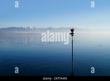 Hafen der Insel Lindau am ruhigen Bodensee oder Bodensee mit den Alpen im Hintergrund an einem schönen Winterabend mit malerischem Himmel Stockfoto