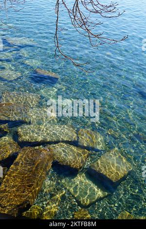 Klares türkisfarbenes Wasser des Bodensees oder Bodensees mit Steinen, Felsblöcken und Kieselsteinen als Hintergrund der Website Stockfoto