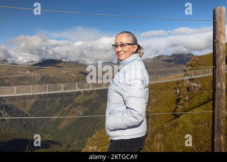 Eine Frau in Sportbekleidung steht am Zaun vor dem Hintergrund einer Metallbrücke in den österreichischen Alpen. Hochwertiges Foto Stockfoto