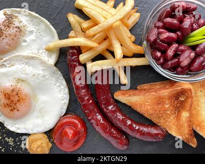 Frühstück auf dunklem Brett mit Bohnen, Eiern, Würstchen, pommes frites und Toast. Draufsicht Stockfoto