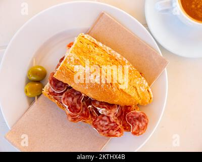 Spanisches Frühstück: Geräuchertes Würstchen-Fuet-Sandwich und Oliven in der Nähe Stockfoto