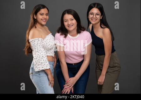 Drei junge Latino-Mädchen lächeln auf grauem Studiohintergrund Stockfoto