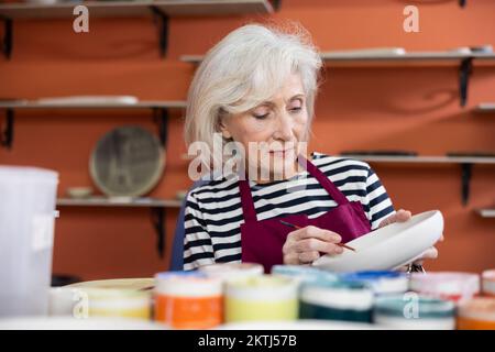 Reife Handwerkerin, die Tonplatten-Acrylfarben im Kunstatelier malt Stockfoto