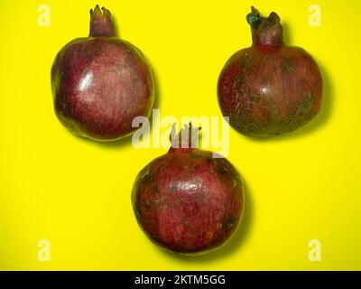 Granatapfel auf Gelb. Saftige Früchte auf gelbem Hintergrund. Ganze Früchte. Drei Granaten. Rohkost-Diät. Saftzutat. Stockfoto