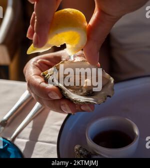 Die junge Frau in weißem Kleid isst im französischen Restaurant frische, lebende Creuze-Austern mit marinierten Zwiebeln und Meeresfrüchte Stockfoto