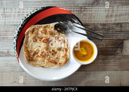 Blick von oben auf einen einfachen roti Canai ohne Schnickschnack mit Dhal Curry auf einem Holztisch Stockfoto
