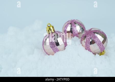 Rosa glitzernde Weihnachtskugeln liegen im Schnee. Stockfoto