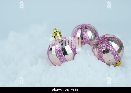 Rosa glitzernde Weihnachtskugeln liegen im Schnee. Stockfoto