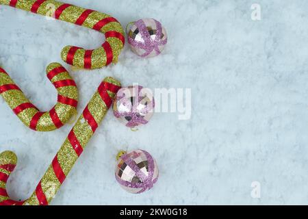 Goldene und rote Zuckerstangen mit glitzernden Weihnachtskugeln im Schnee. Stockfoto