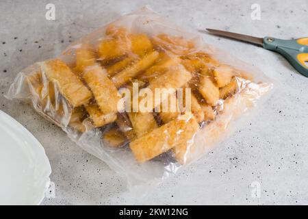 Panierte Fischstäbchen gefroren. Plastiktüte mit Fischstäbchen in knuspriger goldener Panade auf dem Küchentisch Stockfoto