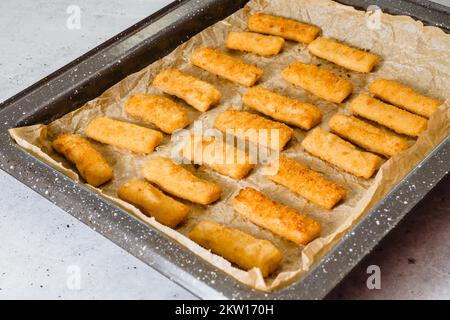 Backpfanne mit Fischstäbchen nah auf dem Küchentisch. Knusprig köstlich, leicht paniert mit Panko-Brotkrumen Fischstäbchen Stockfoto