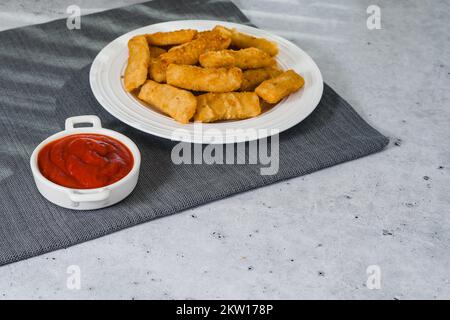 Fischstäbchen in einer knusprigen goldenen Panade und einer Schüssel Ketchup nahe am Küchentisch, Kopierraum Stockfoto
