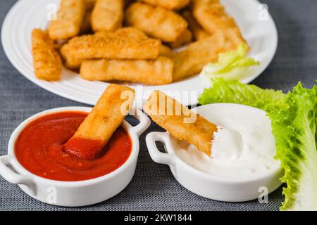 Fischstäbchen in einer knusprigen goldenen Panade mit Ketchup und griechischer Joghurt-Dipping-Sauce aus nächster Nähe Stockfoto