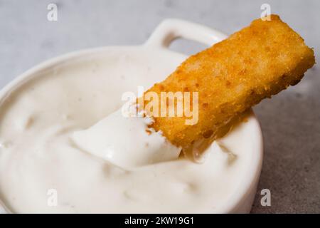 Knusprige panierte Fischstäbchen aus wild gefangenem Alaska-Pollock, getaucht in griechischer Joghurt-Knoblauch-Dip-Sauce, dicht auf dem Küchentisch Stockfoto