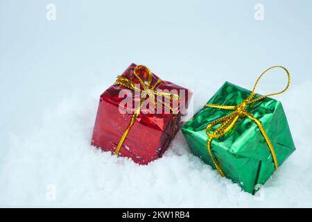 Rot-grünes Geschenk mit Metallschnur auf dem Schnee. Stockfoto