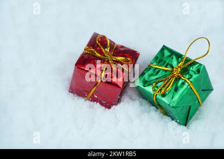 Rot-grünes Geschenk mit Metallschnur auf dem Schnee. Stockfoto