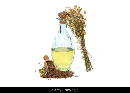 Leinsamenöl in Glasdekanter und Leinsamen in Holzschaufel in der Nähe von Flachsbäumen, isoliert auf weißem Hintergrund. Linum usitatissimum (Gemeiner Flachs) Stockfoto