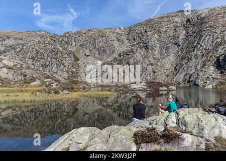 Zwei Wanderer machen eine Pause am Etang d'Arbu auf dem Aufstieg des Pic des Trois seigneurs, Ariège, Pyrenäen, Frankreich, EU Stockfoto