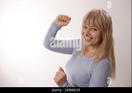 Die Frau zeigt zwei Daumen hoch, sie ist glücklich, tanzt sich drehende Anime vor der Kamera. Positive, hübsche Frau zeigt zwei Hände, Daumen hoch, Zahnlächeln Stockfoto