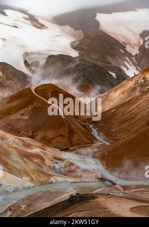 Brücke und dampfende Bäche zwischen farbenfrohen Rhyolitenbergen und Schneefeldern, geothermisches Gebiet Hveradalir, Kerlingarfjöll, isländische Highlands, Icel Stockfoto