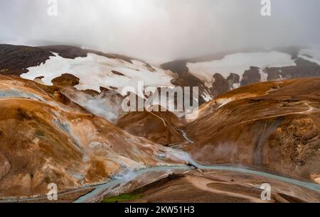 Brücke und dampfende Bäche zwischen farbenfrohen Rhyolitenbergen und Schneefeldern, geothermisches Gebiet Hveradalir, Kerlingarfjöll, isländische Highlands, Icel Stockfoto