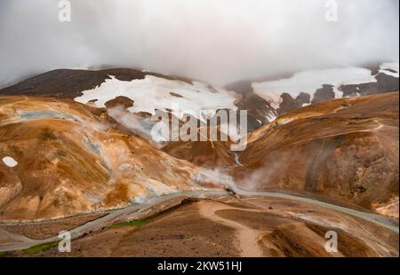 Brücke und dampfende Bäche zwischen farbenfrohen Rhyolitenbergen und Schneefeldern, geothermisches Gebiet Hveradalir, Kerlingarfjöll, isländische Highlands, Icel Stockfoto