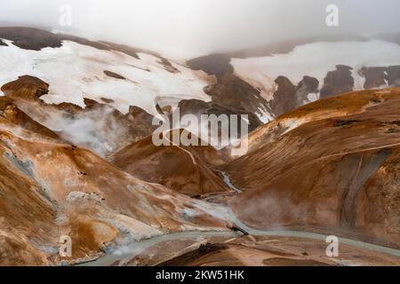 Brücke und dampfende Bäche zwischen farbenfrohen Rhyolitenbergen und Schneefeldern, geothermisches Gebiet Hveradalir, Kerlingarfjöll, isländische Highlands, Icel Stockfoto