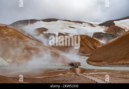 Brücke und dampfende Bäche zwischen farbenfrohen Rhyolitenbergen und Schneefeldern, geothermisches Gebiet Hveradalir, Kerlingarfjöll, isländische Highlands, Icel Stockfoto