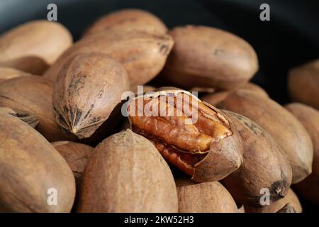 Nahaufnahme von Pekannüssen in der Schale, eine Nuss gerissen, Hintergrund Stockfoto