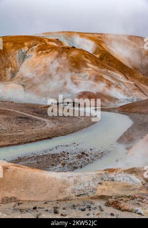 Brücke und dampfende Bäche zwischen farbenfrohen Rhyolitenbergen und Schneefeldern, geothermisches Gebiet Hveradalir, Kerlingarfjöll, isländische Highlands, Icel Stockfoto