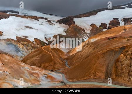 Brücke und dampfende Bäche zwischen farbenfrohen Rhyolitenbergen mit Schneefeldern, geothermischer Region Hveradalir, Kerlingarfjöll, isländischen Hochland, Eis Stockfoto