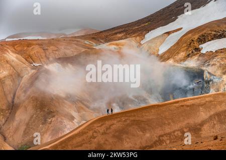 Wanderer auf einem farbenfrohen Rhyolitenberg, dampfende heiße Quellen im Hintergrund, geothermisches Gebiet Hveradalir, Kerlingarfjöll, isländische Highlands, Island, E Stockfoto