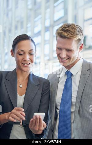 Apps, die Unternehmen bei der Umsatzoptimierung unterstützen. Zwei Geschäftskollegen stehen und schauen sich etwas auf einem Mobiltelefon an. Stockfoto