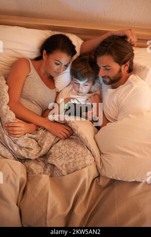 Märchenzeit im modernen Zeitalter. Eine Aufnahme eines kleinen Jungen, der ein Tablet benutzt, während er im Bett liegt. Stockfoto