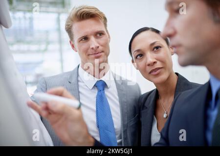 Er ist ein genialer Geschäftsstratege. Ein Geschäftsmann, der ein Diagramm auf einem Flipchart zeichnet, während seine Kollegen daneben stehen. Stockfoto