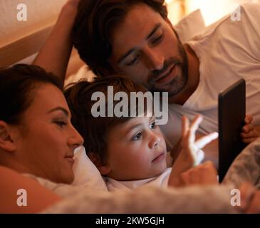 Märchenzeit im modernen Zeitalter. Eine Aufnahme eines kleinen Jungen, der ein Tablet benutzt, während er im Bett liegt. Stockfoto