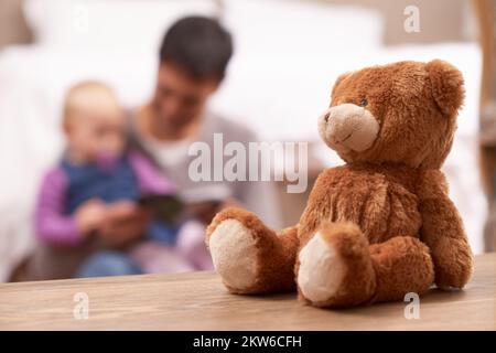 Im Schlafzimmer ist alles ruhig, während Dad eine Geschichte liest. Ein junger Vater, der seinem kleinen Mädchen ein Märchenbuch vorliest. Stockfoto