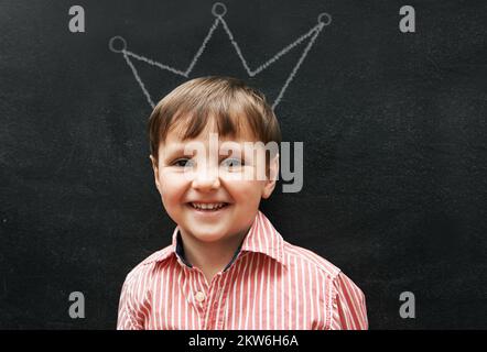 Zeichnen macht so viel Spaß. Studioaufnahme eines entzückenden kleinen Jungen mit Kreidezeichnungen hinter ihm. Stockfoto