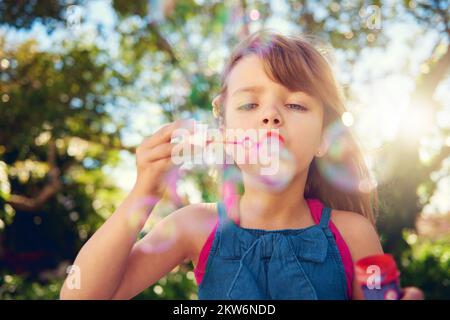 Die Kindheit dauert das ganze Leben. Ein süßes junges Mädchen, das draußen Blasen bläst. Stockfoto