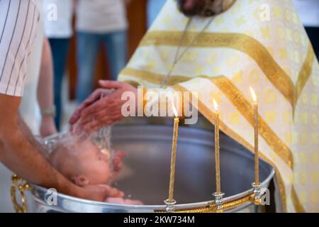 Verschwommener Ritus orthodoxer Taufe vor dem Hintergrund brennender Kerzen. Stockfoto