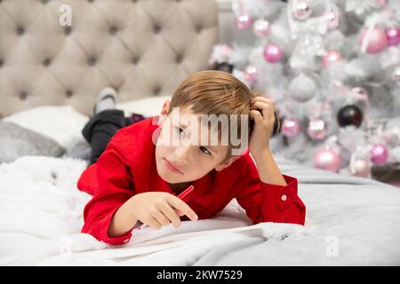 Der kleine schreibt einen Brief an den Weihnachtsmann, denkt über Weihnachtsgeschenke nach. Stockfoto