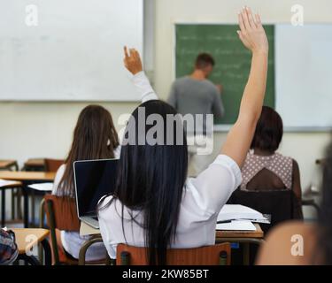 Ich habe eine Frage... Eine Studentin hebt ihre Hand, um während des Unterrichts eine Frage zu stellen. Stockfoto