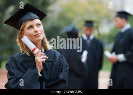 Dieser Abschluss eröffnet so viele Möglichkeiten. Eine attraktive junge Frau, die an die Zukunft denkt, während sie ihren Abschluss hat. Stockfoto